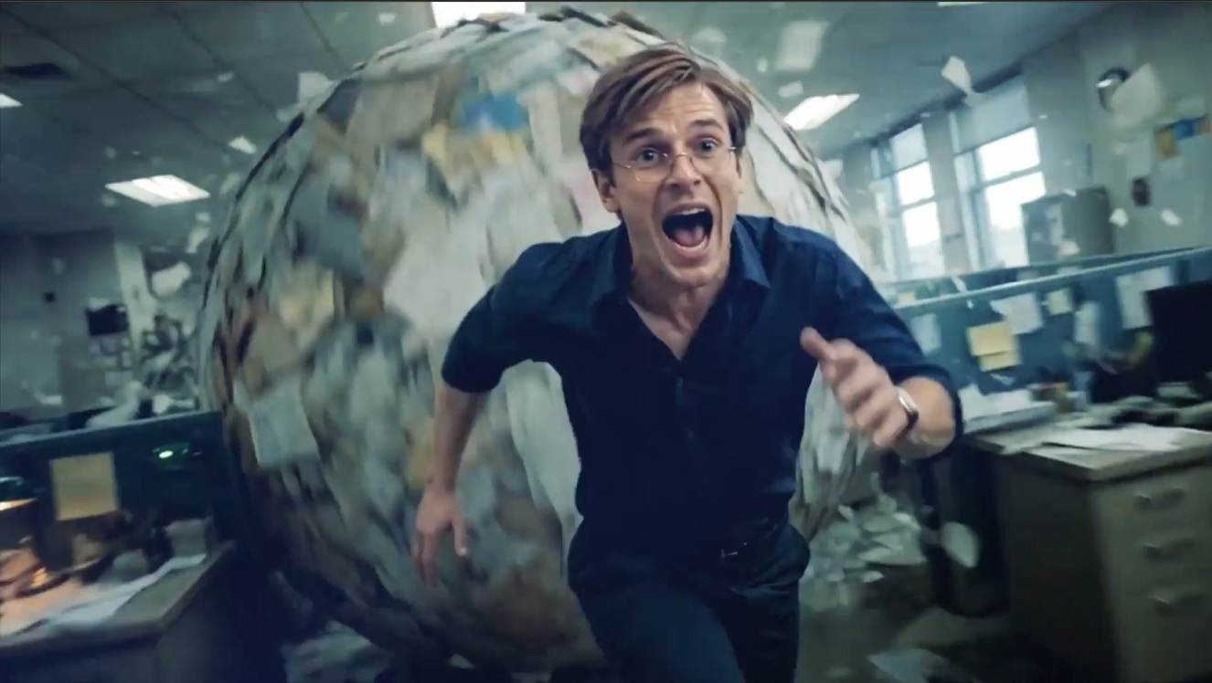An employee running from a giant rolling ball of paperwork